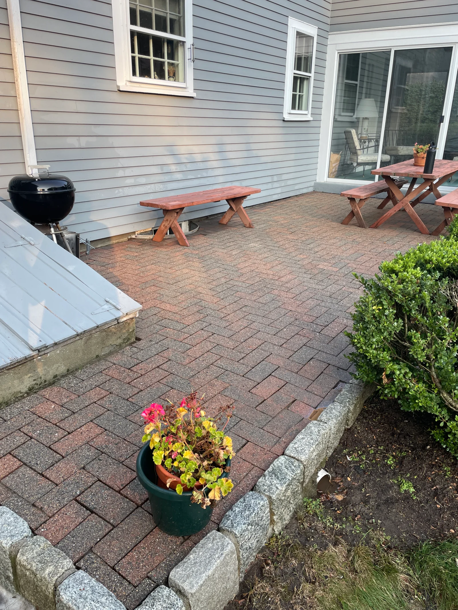 Clean brick paver patio with picnic tables and potted flowers in front of gray house