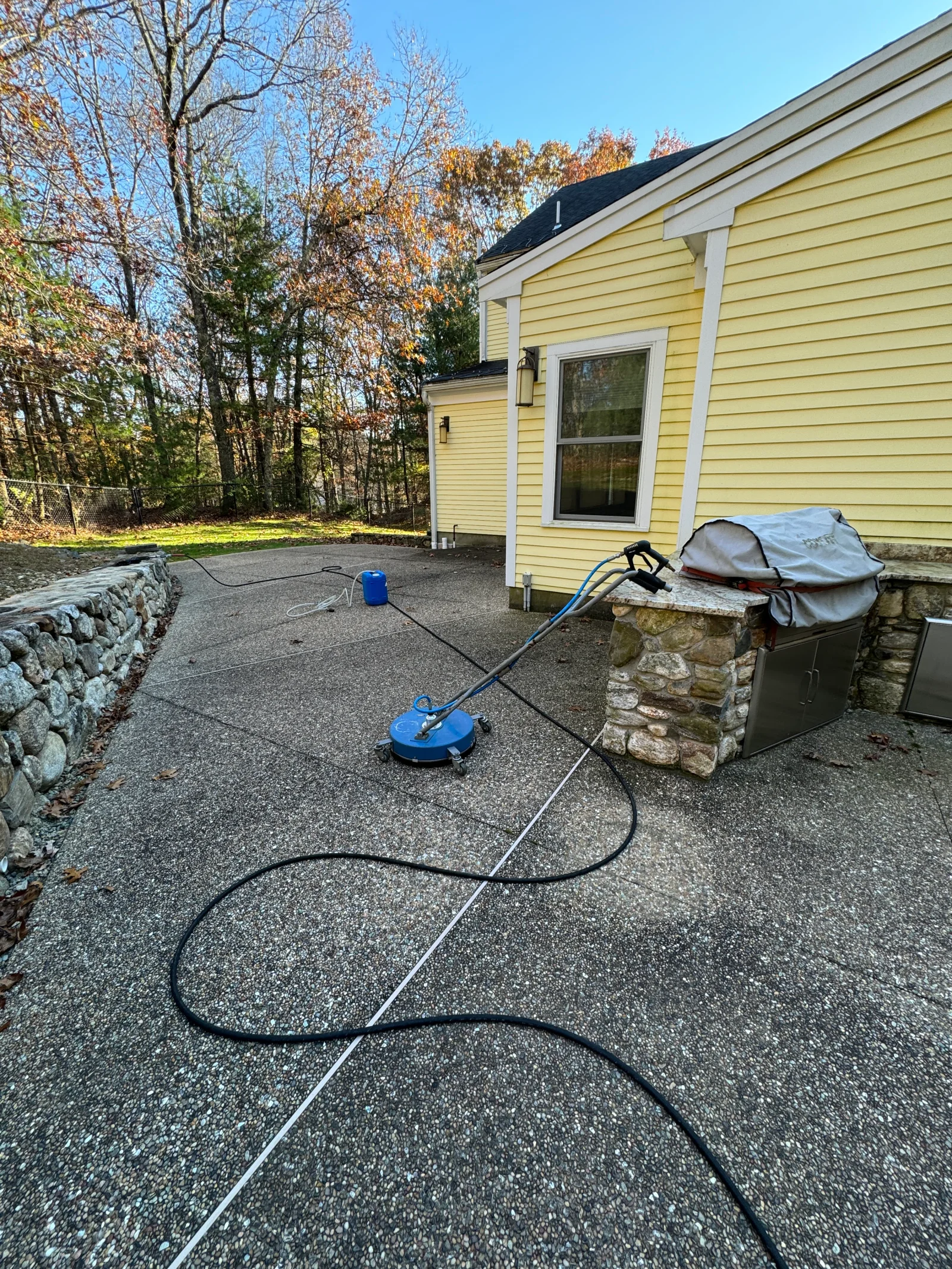 Asphalt driveway pressure washing with blue equipment and hose setup