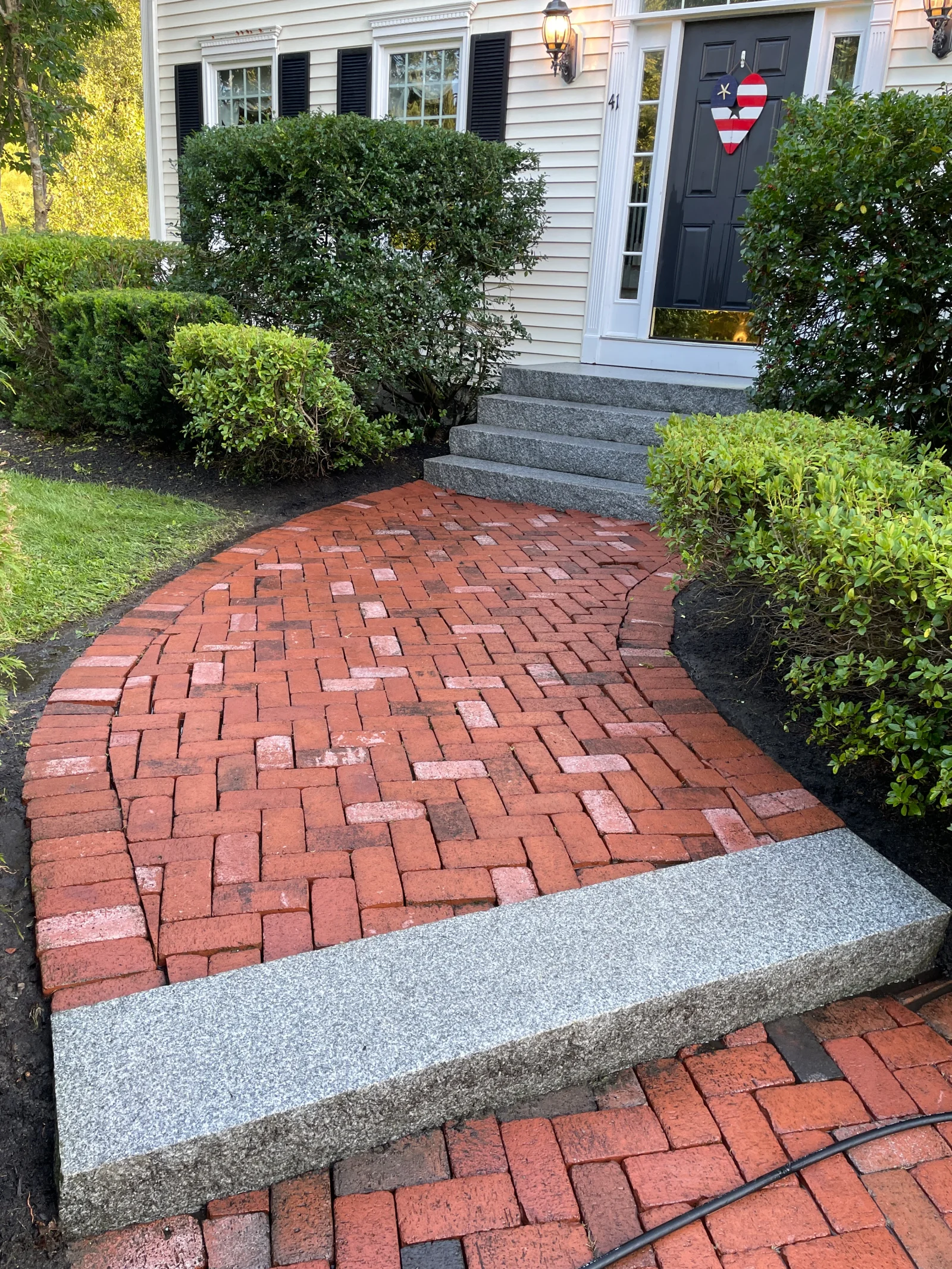 Clean red brick walkway with herringbone pattern and granite step edging leading to home entrance