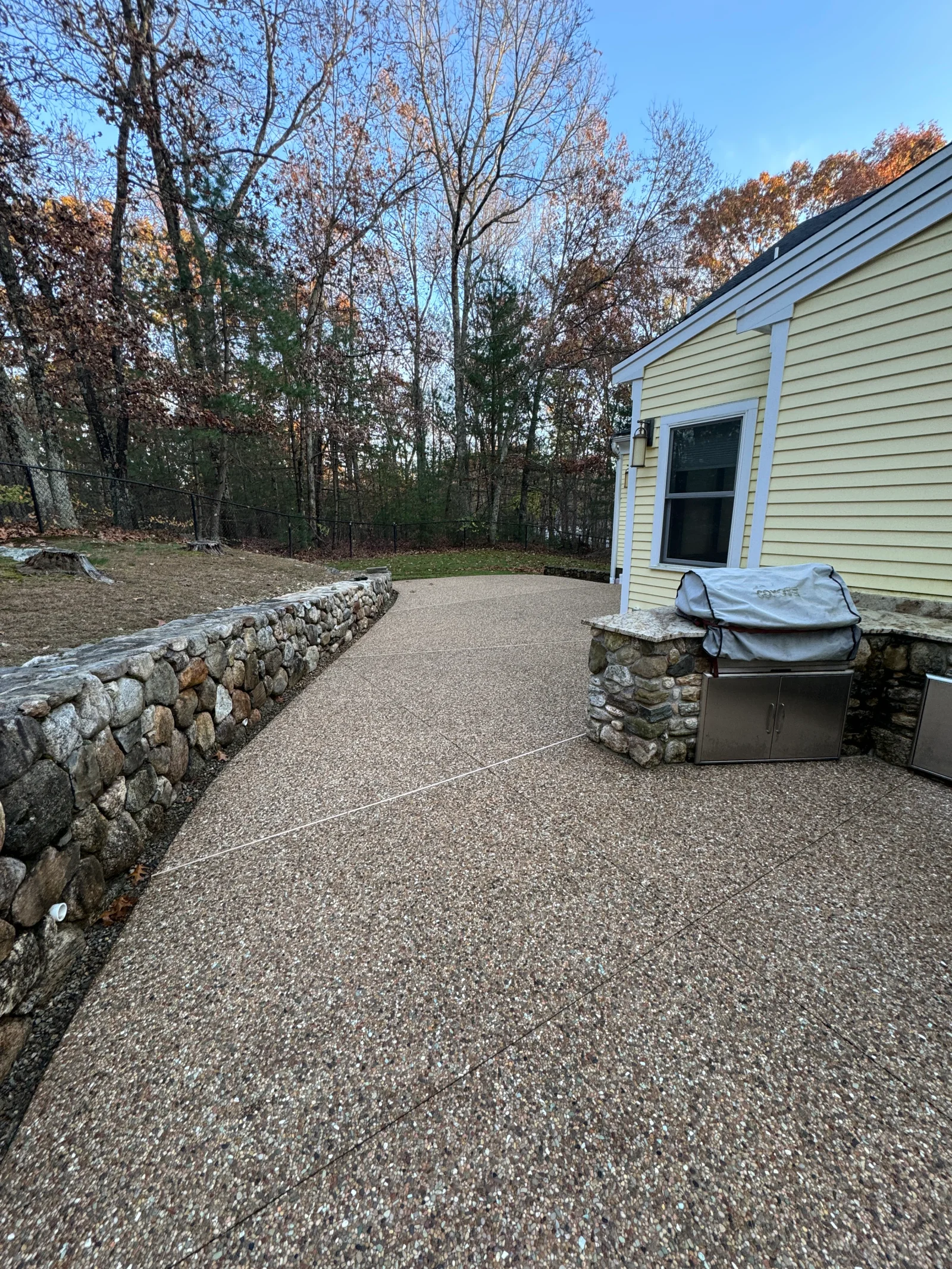 Clean concrete patio with stone retaining wall and outdoor kitchen area