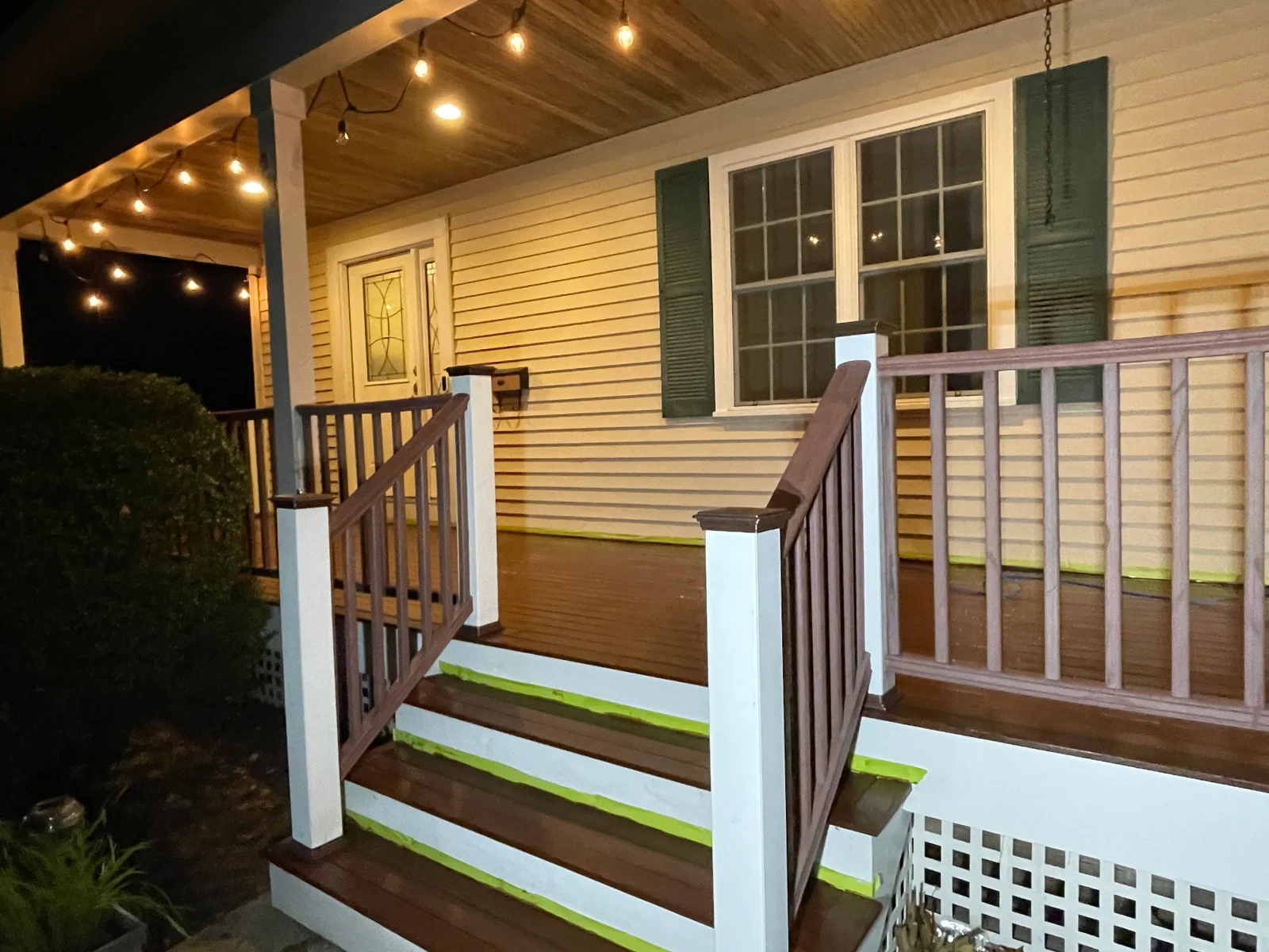 Pressure-washed residential deck with white trim, dark brown boards, and cream vinyl siding at night with accent lighting
