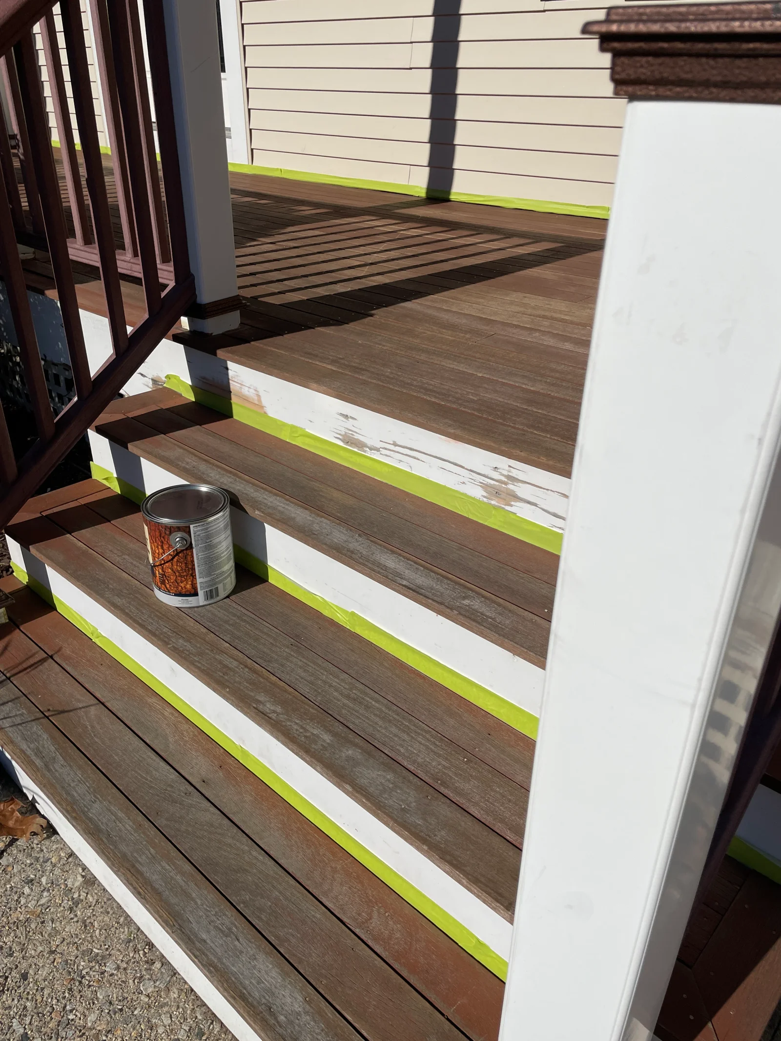Brown stained composite deck with white trim and yellow tape on stairs, freshly sealed