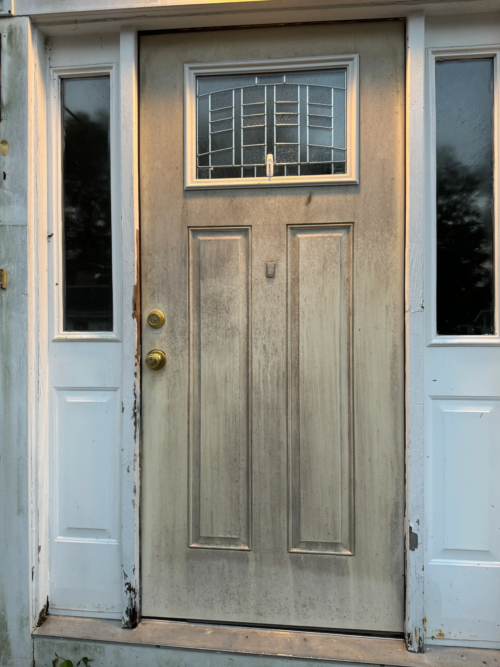 Clean wood entry door with transom window and brass hardware, flanked by white sidelights